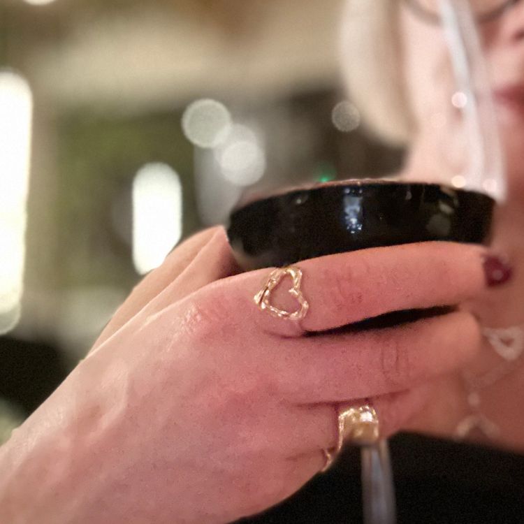 A hand holding a cup wearing a gold heart ring from Lulu and Boo Jewellery